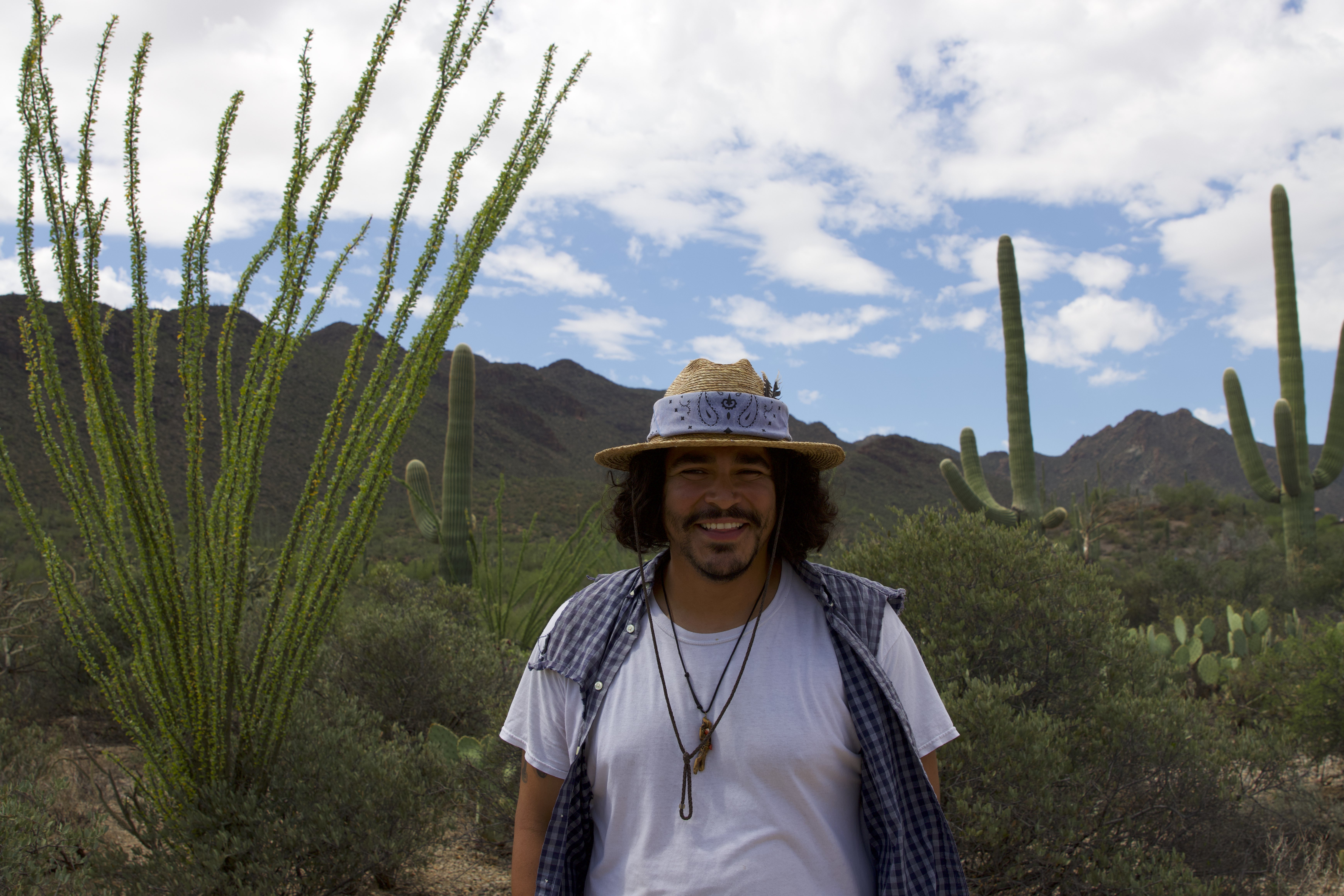 Isaac Silva wearing a hat and white shirt outside under a sunny sky with desert scenery in the background outside under a sunny sky with desert scenery in the background