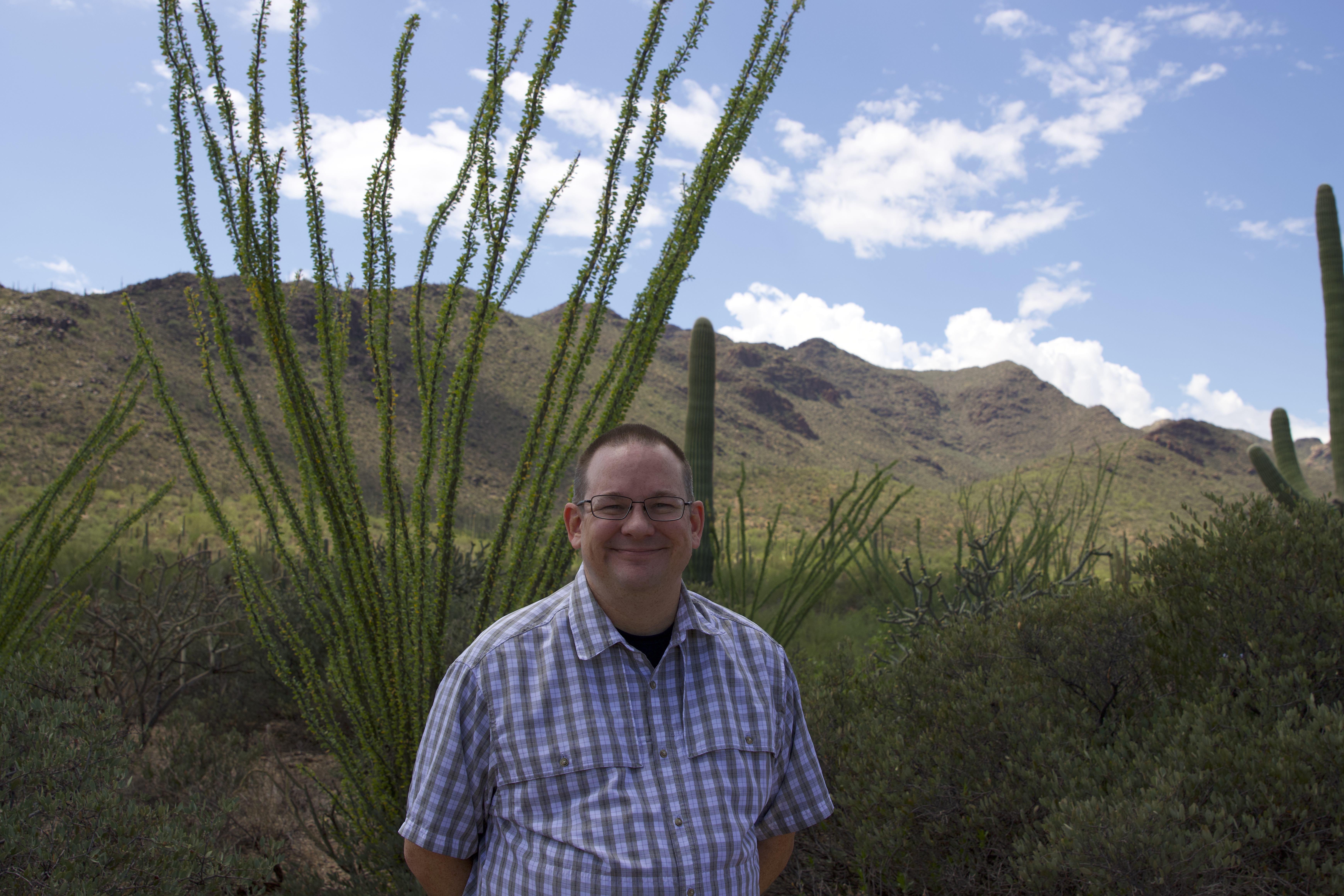 colin waite outside under a sunny sky with desert scenery in the background