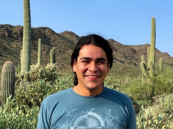 Picture of Isaac Silva, staff member, in a desert setting.  Isaac is smiling with his hair pulled back.