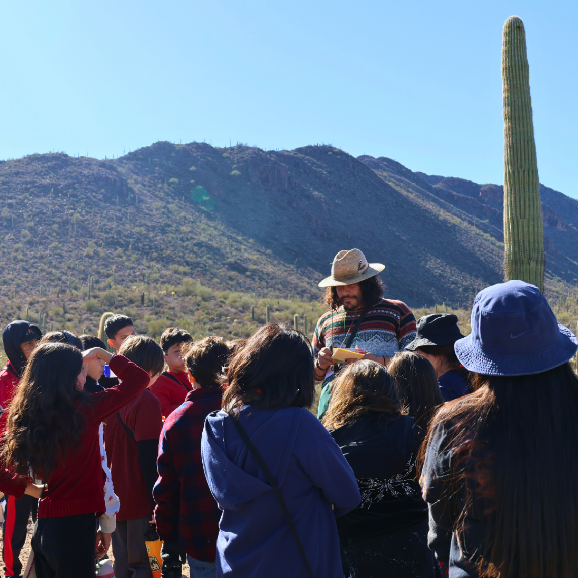 group leader speaking to a group of kids, mountain scape and sahuaro as a backdrop