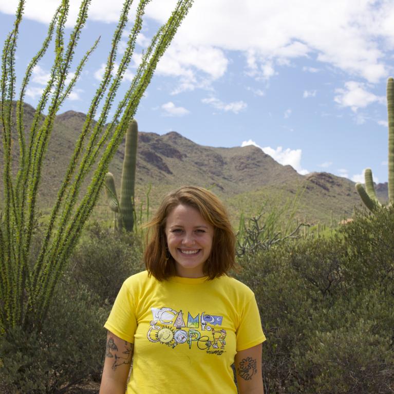 Aliya McDonald wearing a yellow shirt outside under a sunny sky with desert scenery in the background