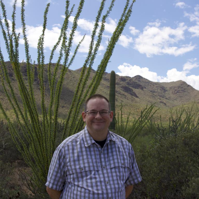 colin waite outside under a sunny sky with desert scenery in the background