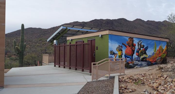 Colorful mural on a small building at the Cooper Center, featuring cartoon desert animals in hiking gear, set against a backdrop of mountains and cacti.