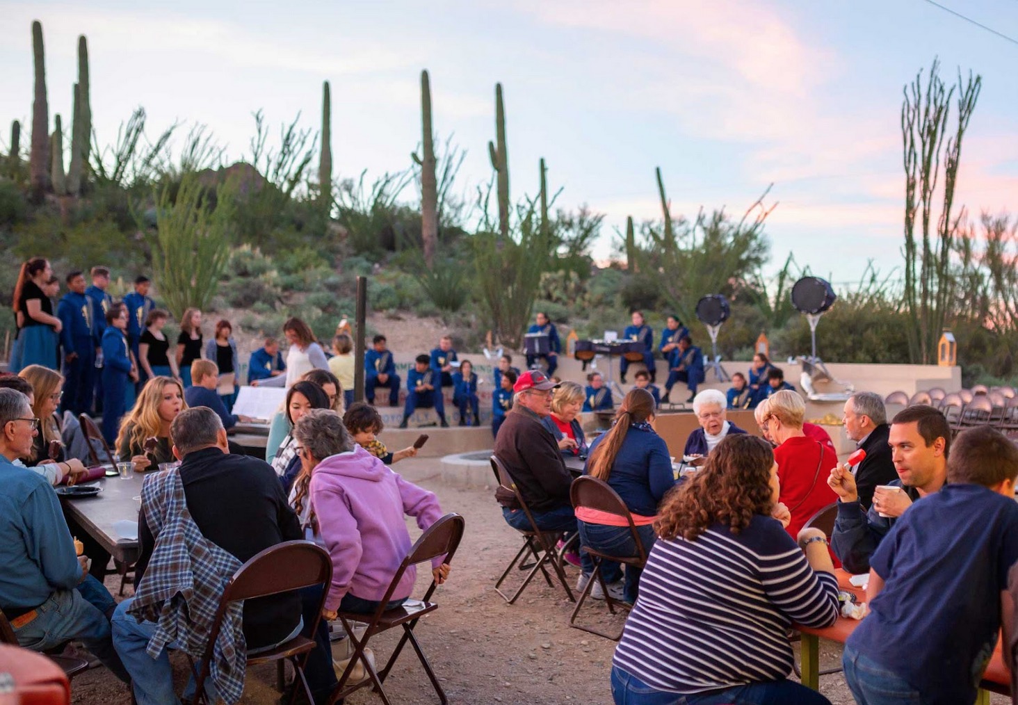 Crowd seated at tables eating with desert in background.  Evening light.
