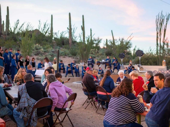 Crowd seated at tables eating with desert in background.  Evening light.
